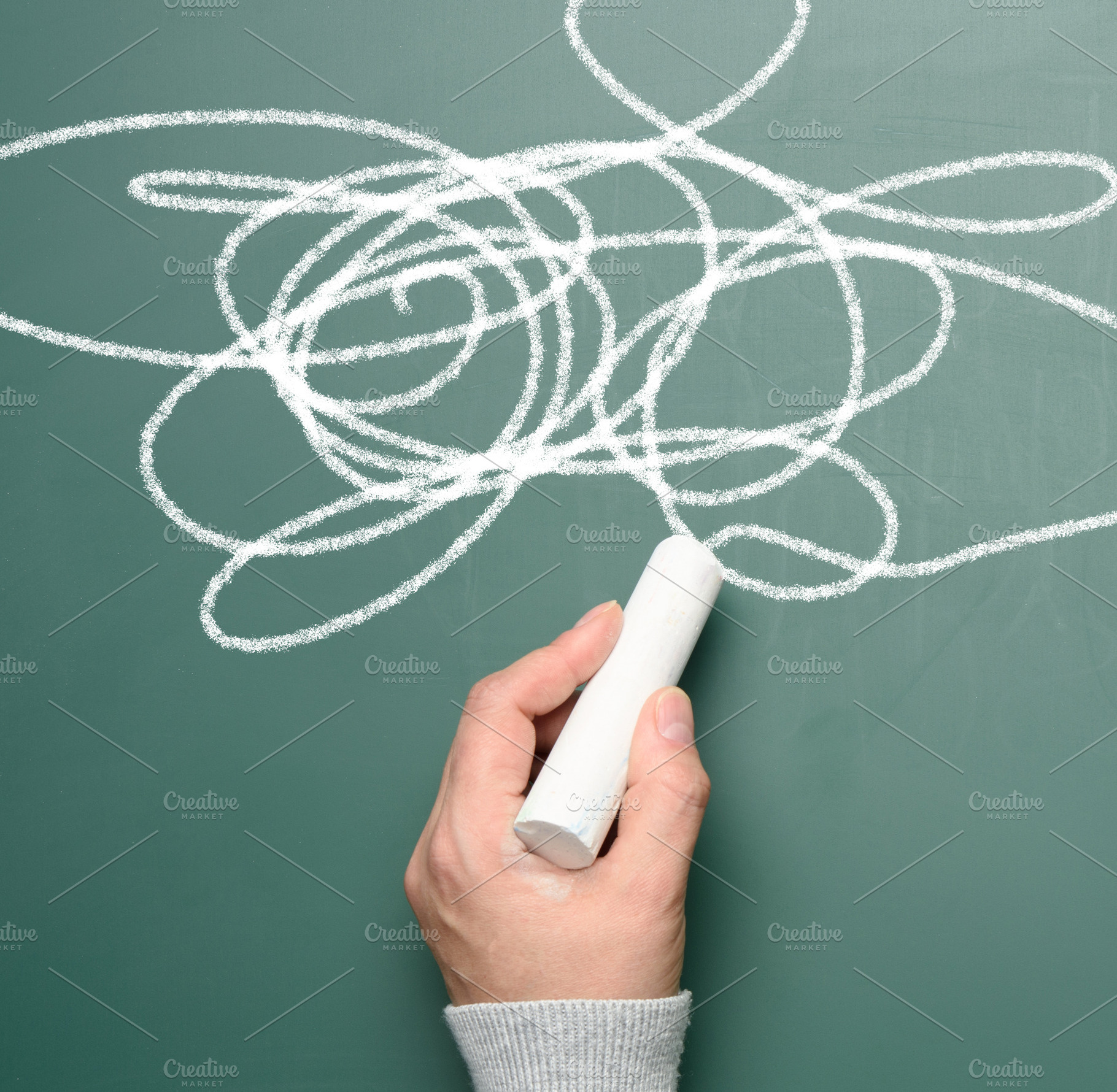 A hand draws random lines with white chalk on a green board, an Abstract Photo by ndanko