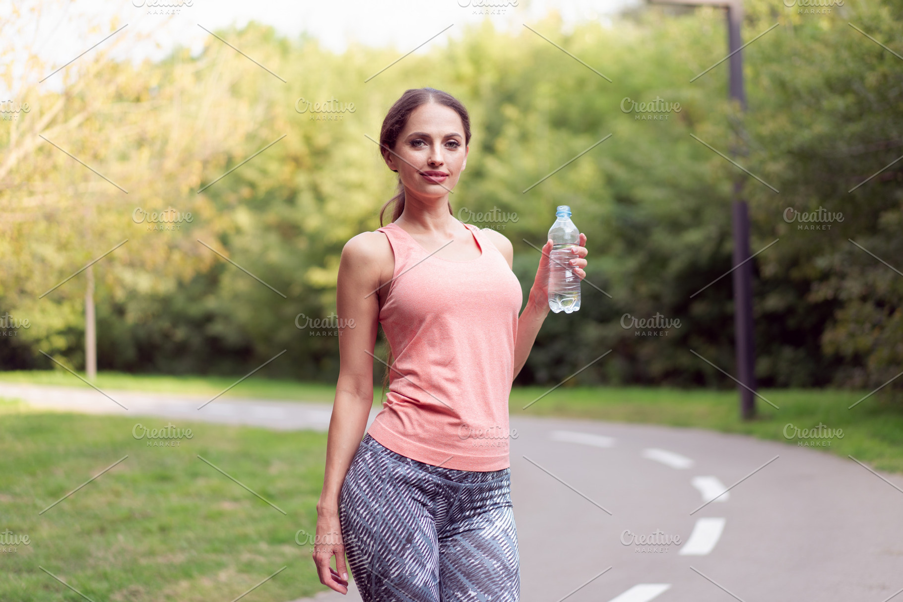 Athletic woman standing running track in summer park drink water after running, a Person Photo by andreonegin market