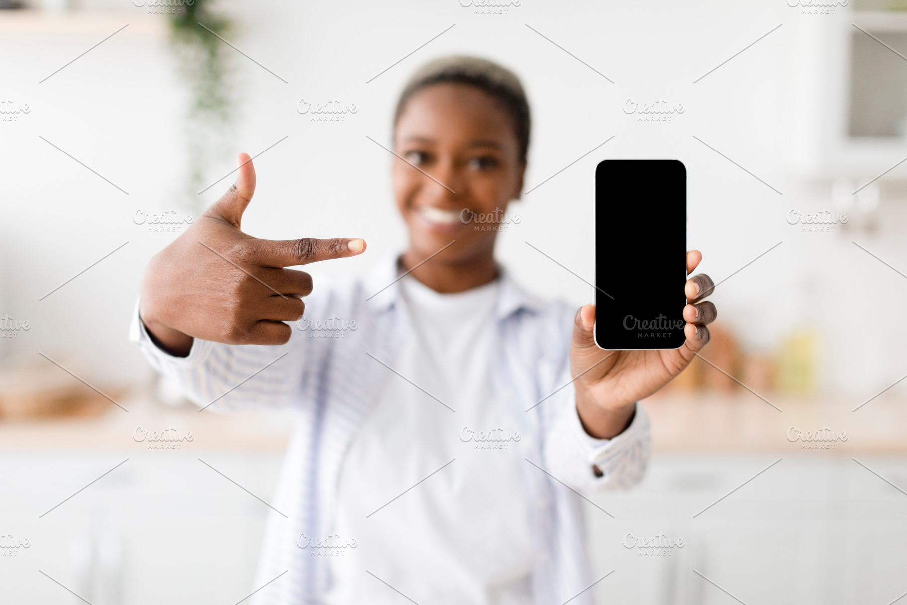 Cheerful young black woman shows on smartphone with blank screen at scandinavia, a Person Photo by Prostock-Studio