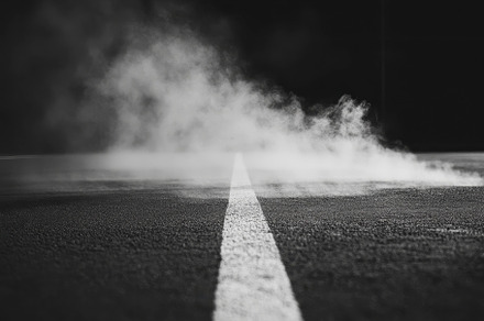 Smoke rising along a dark asphalt ro, a Photo by Tanuart