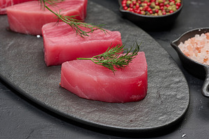 Raw piece of tuna with a sprig of dill on a black board, a Food & Drink Photo by ndanko