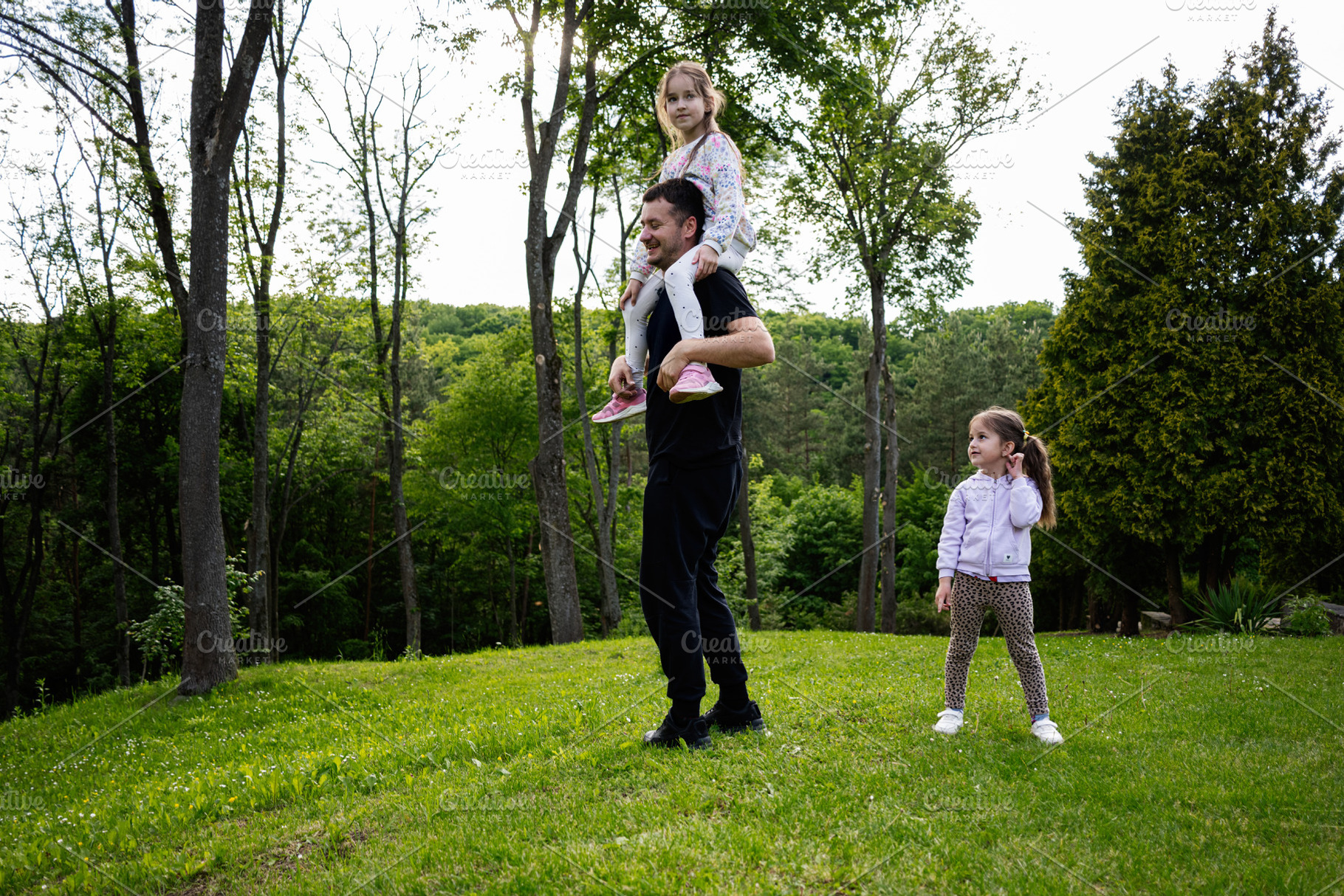 Father playing outdoors with his daughters in a lush green forest setting, a Person Photo by AS photostudio