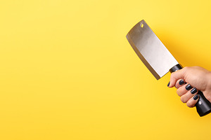 Close-up of a hand gripping a meat cleaver against a vibrant yel, a Food & Drink Photo by Ales Munt