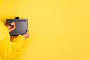 Person in yellow hoodie drawing on a graphic tablet with stylus, a Person Photo by Ales Munt