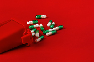 Green and white capsules scattered near a red medical container on bright red b, a Health & Medical Photo by Ales Munt
