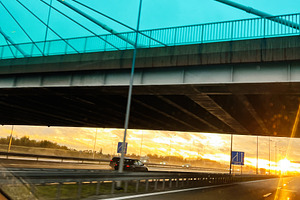Vehicles on a highway at sunrise viewed from inside a car under a turquoise bri, a Photo by AS photostudio