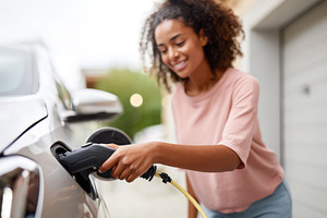 Woman charging electric vehicle at home, a Person Photo by AlyaAnd