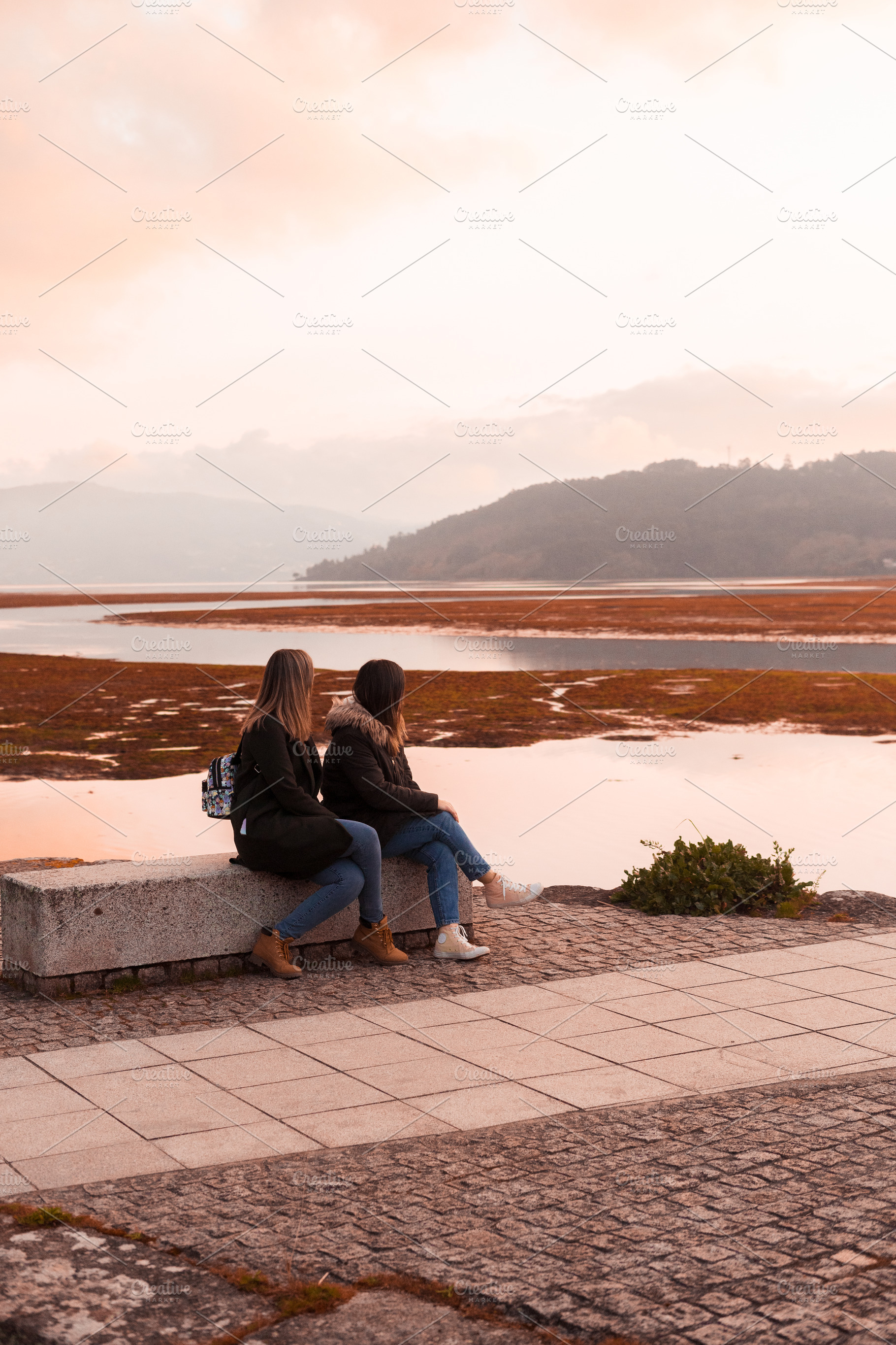 Two female friends sitting on a bench, a Person Photo by rubenchase