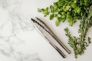 Elegant tongs resting beside herbs, a Photo by Pavel_design