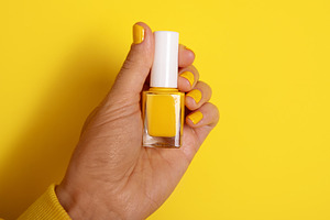 Hand holding a yellow nail polish bottle against a matching yell, a Beauty & Fashion Photo by Ales Munt