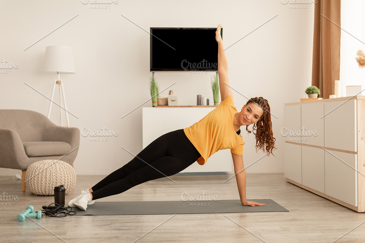 African Female Exercising Doing Side Plank Raising Arm At Home, a Photo by Prostock-Studio (Photo 1 of 2)