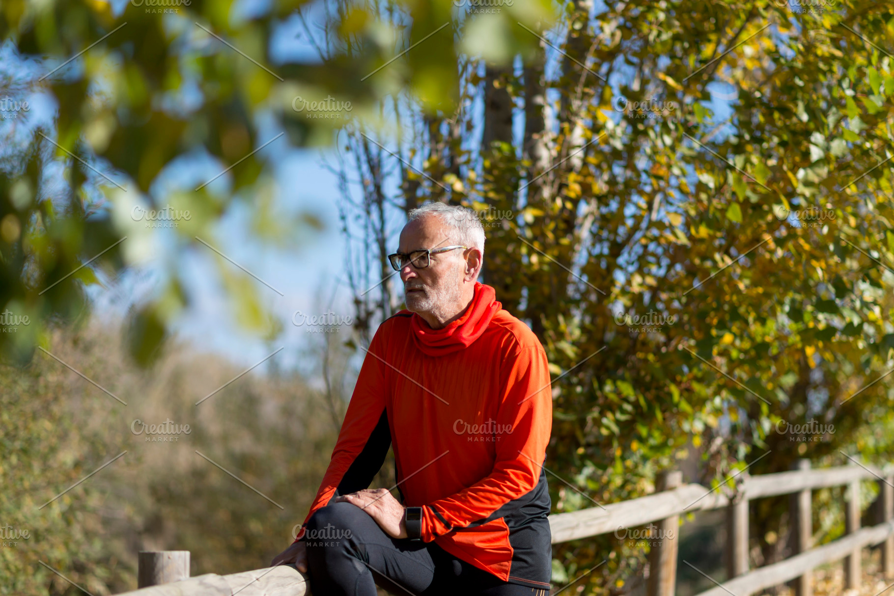 Senior man in bright orange hoodie resting on wooden fence, a Sports & Recreation Photo by RF Images