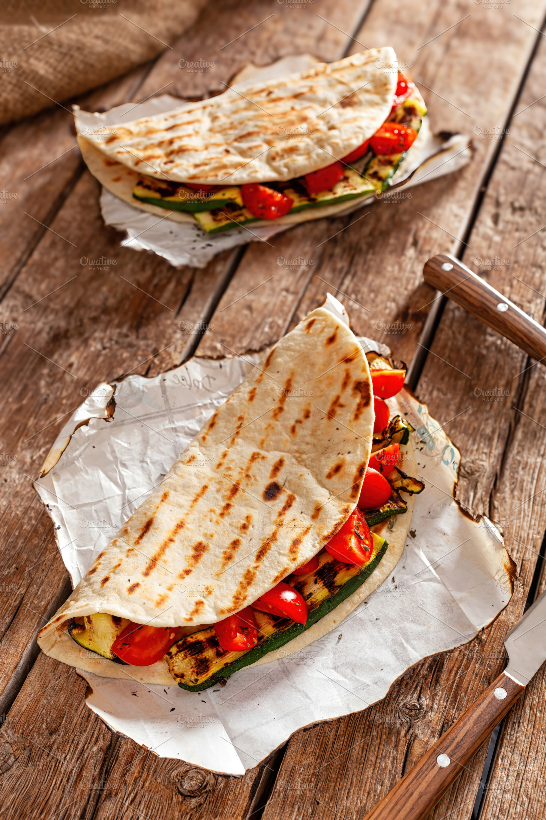 Piadina with grilled zucchini and tomatoes resting on baking paper on wooden ta, a Food & Drink Photo by Antonio Gravante Market