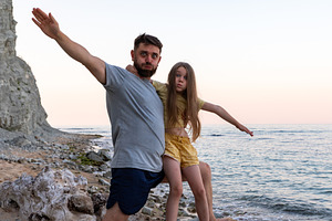Father and daughter posing together on a rocky beach at sunset, arms outstretch, a Person Photo by Ales Munt