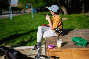 Young boy sitting outdoors enjoying a drink on a sunny day, a Person Photo by AS photostudio