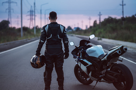A biker stands next to a motorcycle on an asphalt road and looks into the dista, a Transportation Photo by PavelKant