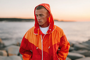 Young man in recycled ocean jacket stands thoughtfully by the shore during suns, a Person Photo by AlyaAnd