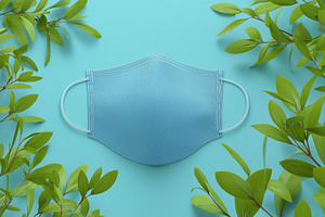 A blue face mask mockup placed on a light blue background surrounded by green l, a Mask Mockup by Textures & Backgrounds