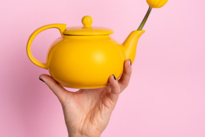 Hand holding a bright yellow teapot with a yellow tulip on a pas, a Holiday Photo by Ales Munt