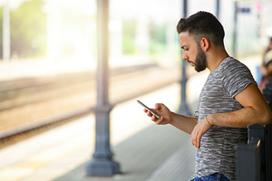 Young man using smartphone while waiting at the train station, an Abstract Photo by Antonio Gravante Market