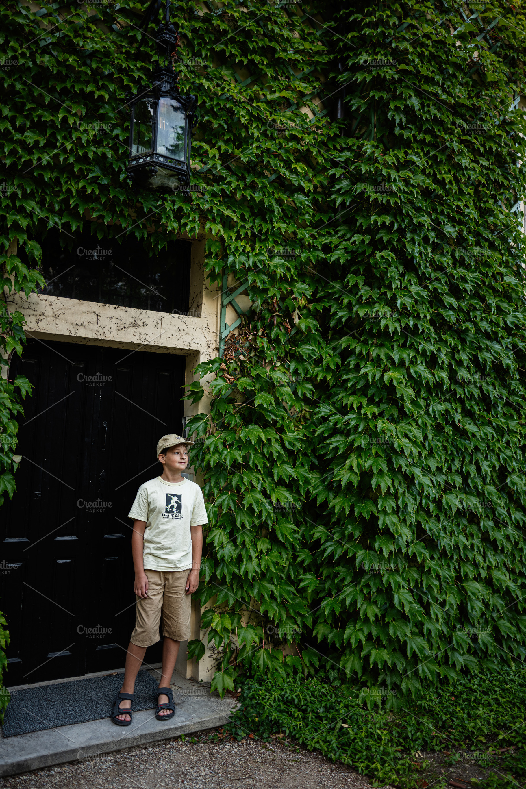 Young boy standing by ivy-covered structure in Lancut, Poland, a Photo by AS photostudio