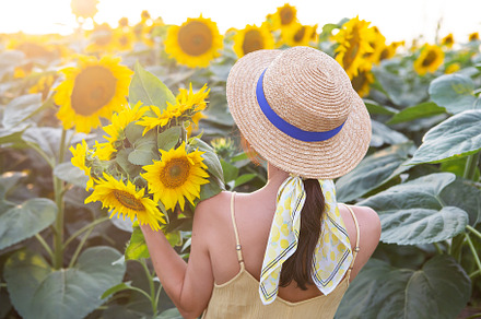 A girl in a straw hat stands with her back and holds in her hands a large bouqu, a Person Photo by Artsaba Family
