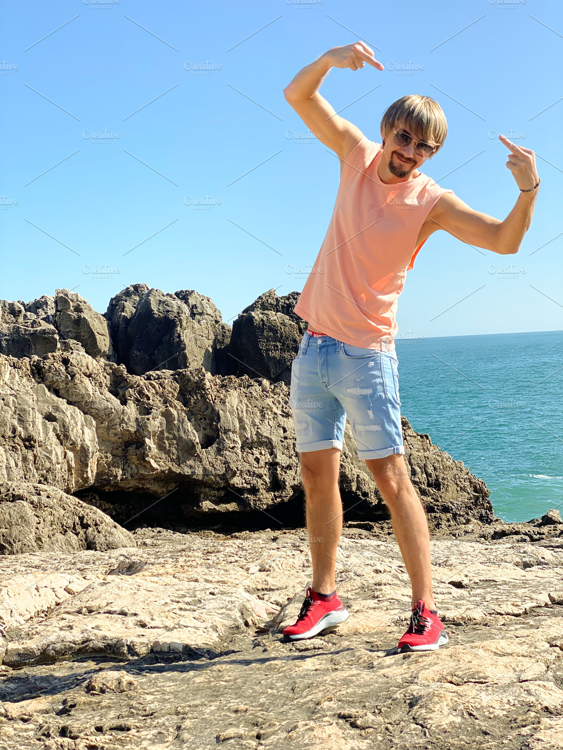 Man in casual summer attire posing playfully on rocky coastal te, a Person Photo by sebastianaraw