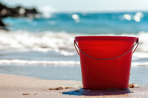Vibrant red bucket rests on sandy, a Photo by Pavel_design