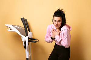 Young woman holding chest in discomfort next to an elliptical tr, a Person Photo by Ales Munt