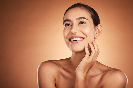 Thinking, beauty and skincare of hispanic woman against a brown studio background. Clean, smooth face skin of a happy woman after cosmetology and dermatology treatment for health and wellness, a Photo by Peopleimages.com