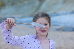 Smiling girl holding a feather on a sandy beach with soft natural light and a b, a Person Photo by Ales Munt