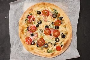 Round pizza with bacon, chicken, olives and cheese on parchment, a Food & Drink Photo by ndanko