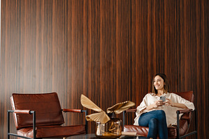 Young smiling woman using cellphone while sitting in armchair indoors