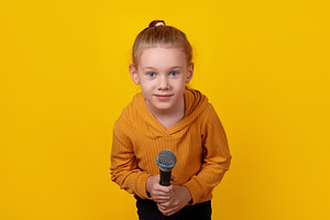 Smiling young girl in yellow hoodie holding a microphone against, a Person Photo by Ales Munt