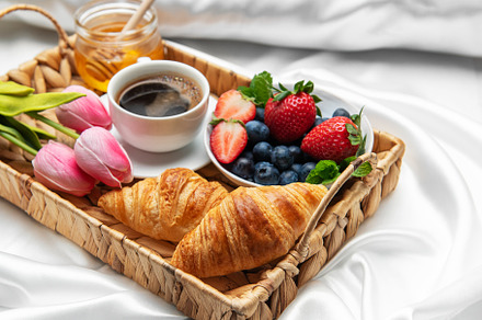 Romantic breakfast in bed with coffee, croissants, berries, hone