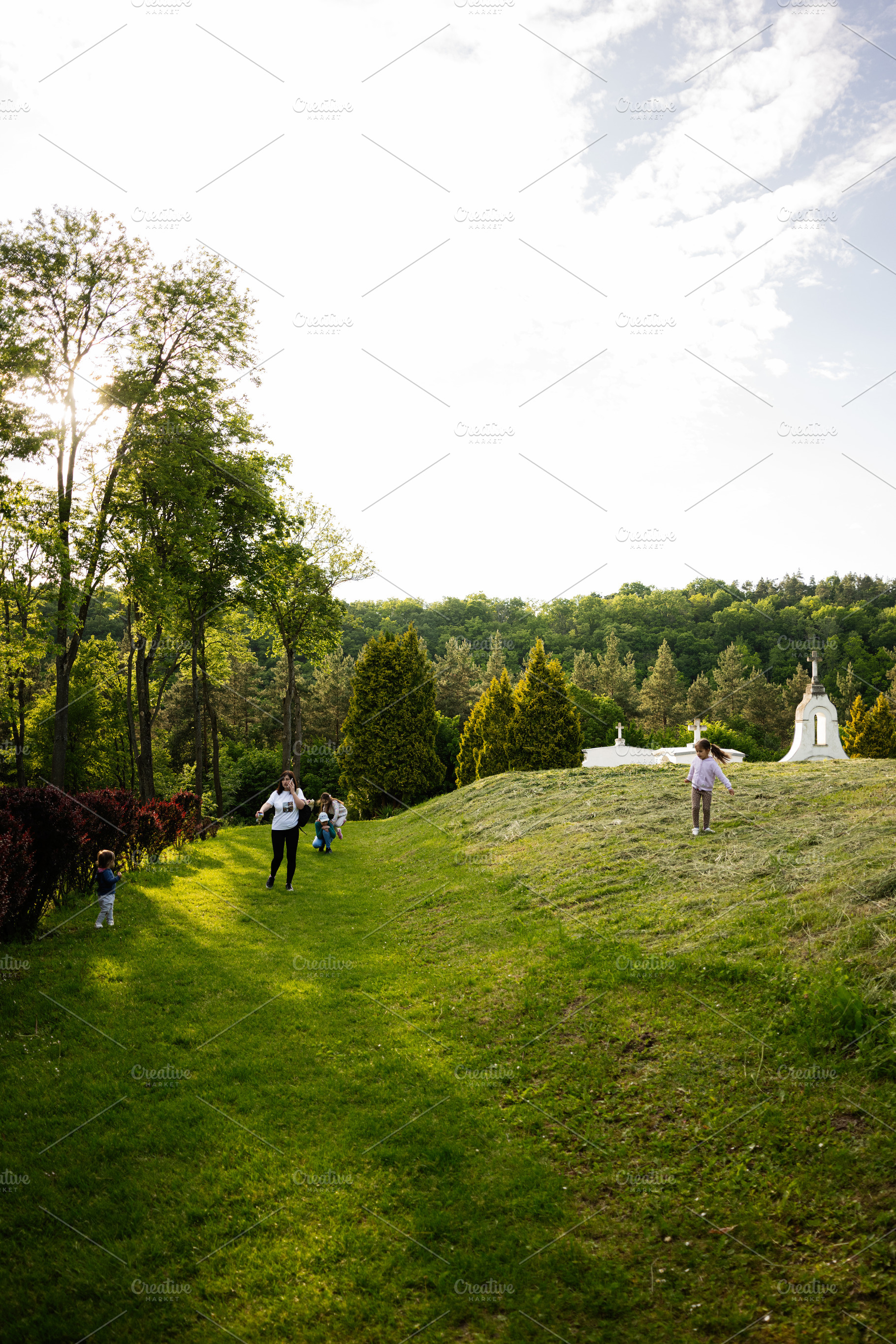 Family enjoying a sunny walk along a lush green park pathway, a Photo by AS photostudio