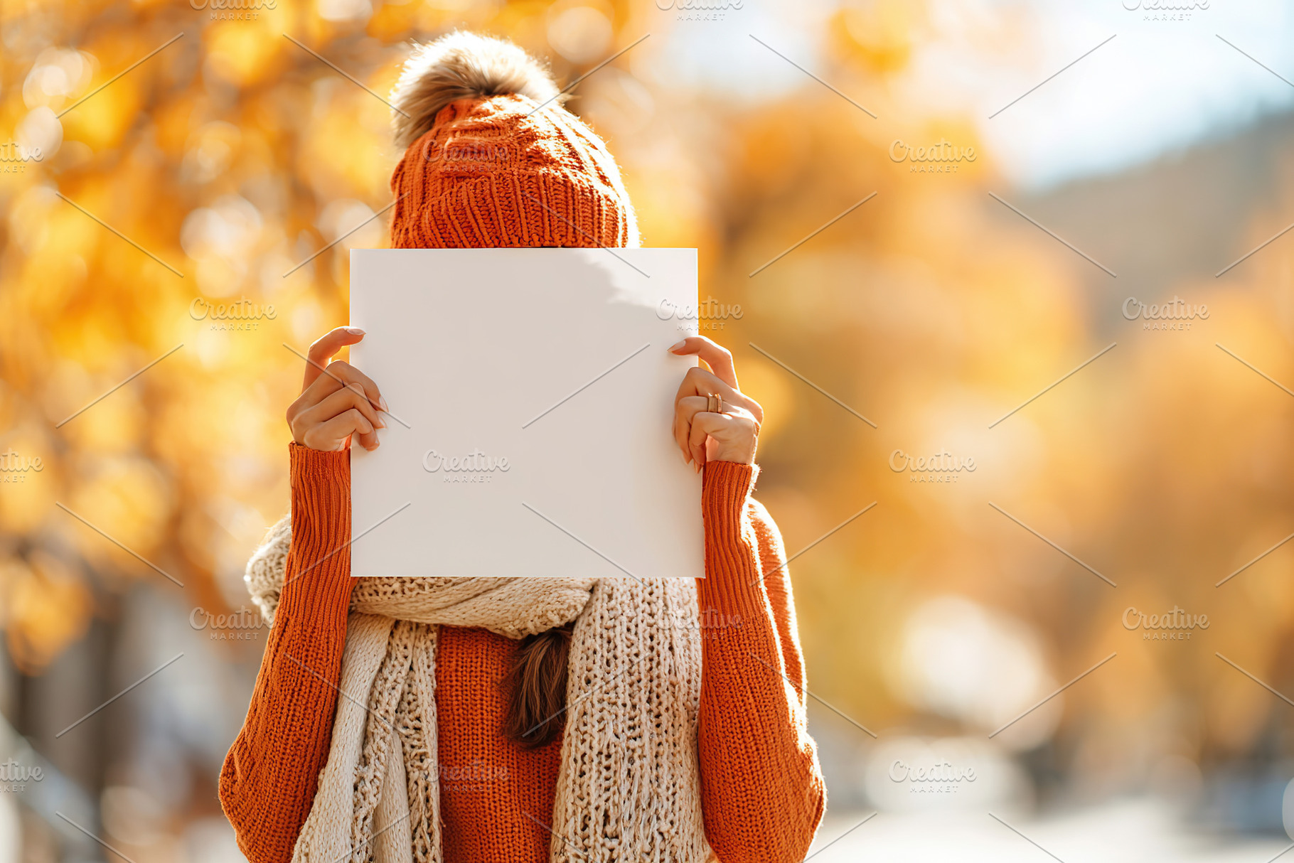 Young woman holding blank poster outdoors in autumn with colorful leaves, a Photo by AlyaAnd