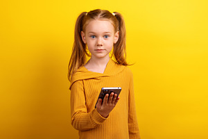 Young girl in a mustard sweater holding a smartphone and looking, a Person Photo by Ales Munt