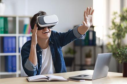 Young Man Wearing VR Glasses Touching Virtual Screen While Sitting At Workplace