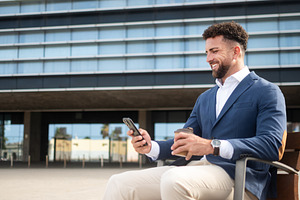 Businessman using smartphone while having coffee outside office, a Business Photo by etorres69