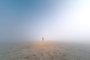 Solitary figure walking through a dense fog in an open, expansive landscape at, a Photo by AlyaAnd