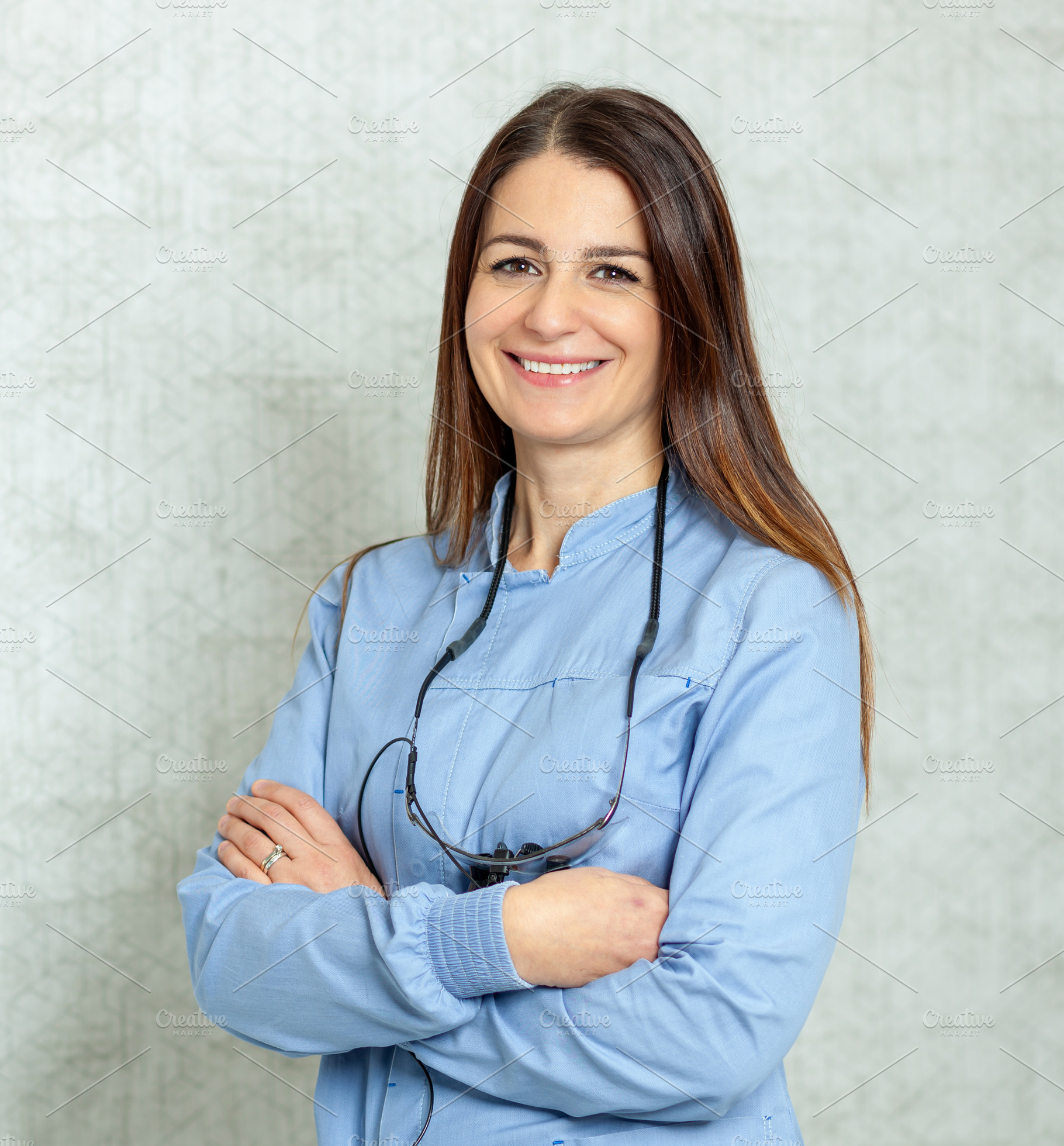 Portrait of smiling female dentist with arms crossed wearing surgical loupes, a Health & Medical Photo by Antonio Gravante Market