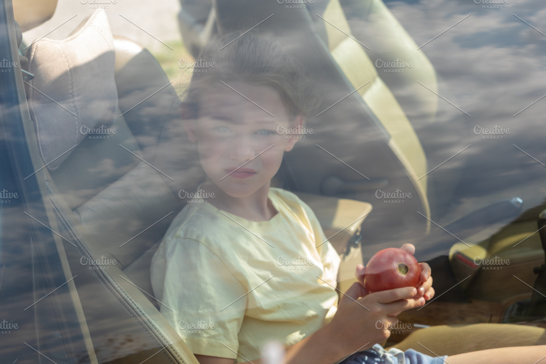 Young girl sitting inside a car, holding an apple, seen through a window with r, a Person Photo by Ales Munt