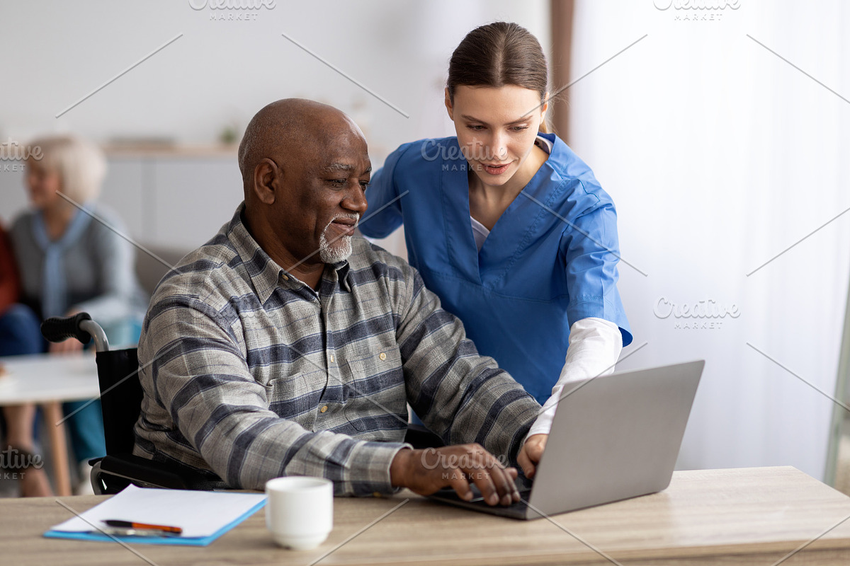 Young woman nurse helping black senior man using laptop, a Photo by Prostock-Studio (Photo 1 of 2)
