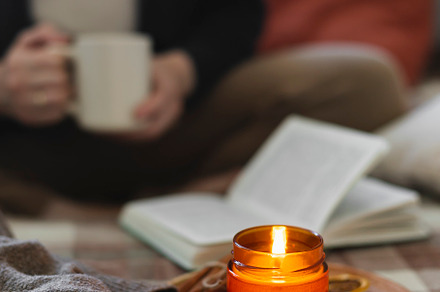 Burning candle on background of young woman holding mug coffee or tea, reading, a Beauty & Fashion Photo by Anikona