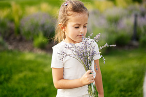 Little girl enjoying the scent of lavender in a sunny garden, a Photo by AS photostudio