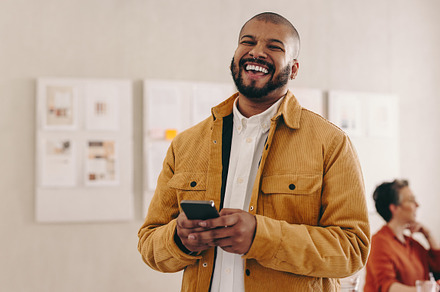 Modern businessman smiling at the camera while holding a smartph
