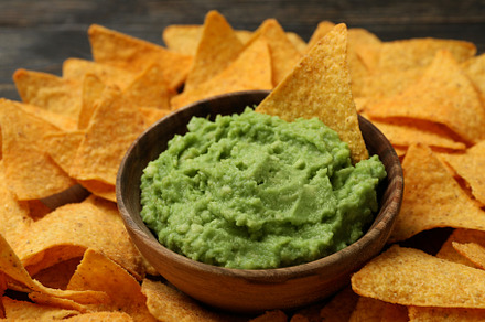 Tray with chips and bowl of guacamole on wooden background, clos, a Photo by AtlasStudio