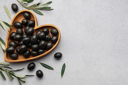 Black olives arranged in heart shaped wooden bowl on gray backgr, a Food & Drink Photo by Olena Rudo