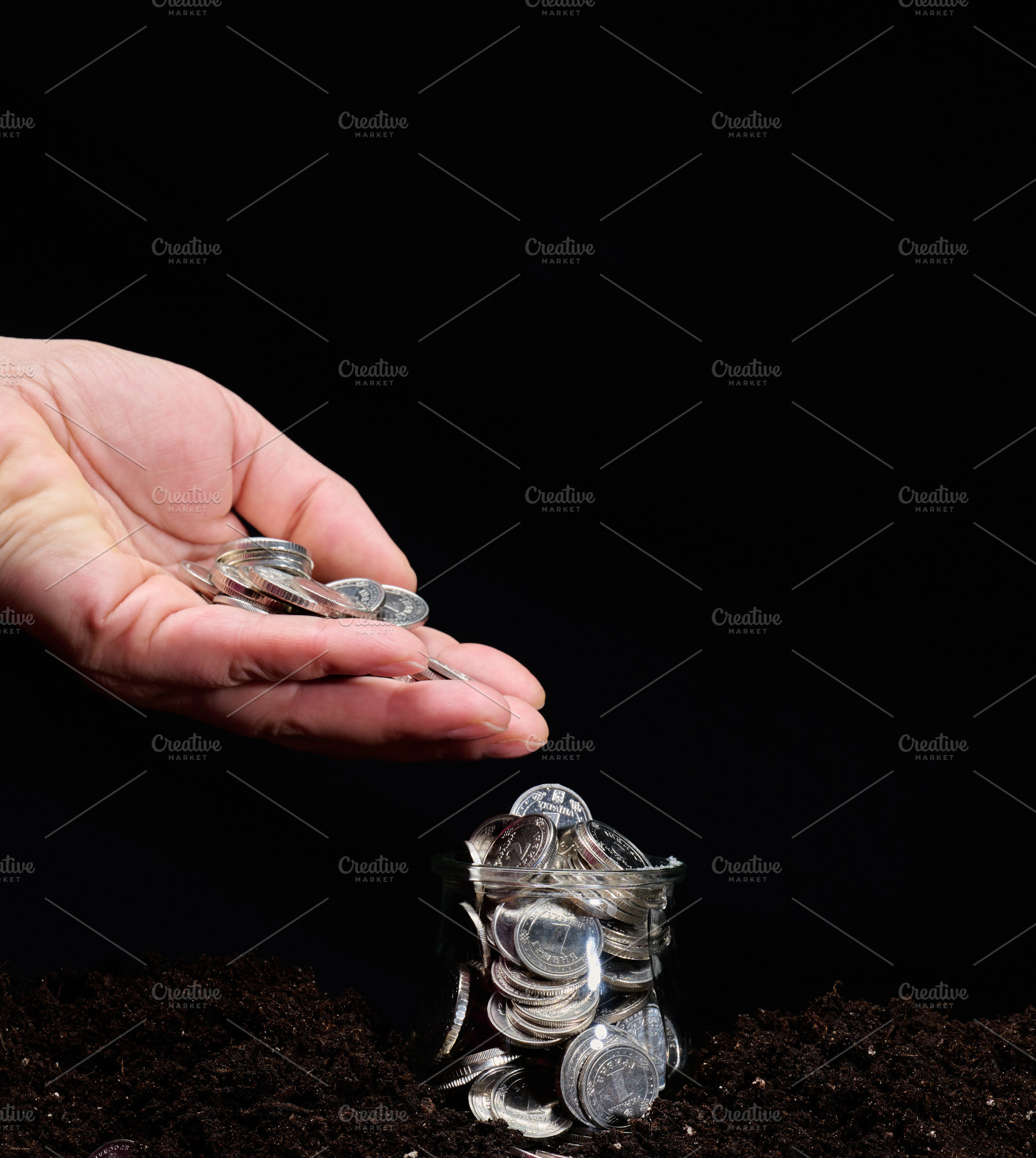 A woman's hand pouring metal coins into a glass jar standing on, a Business Photo by ndanko